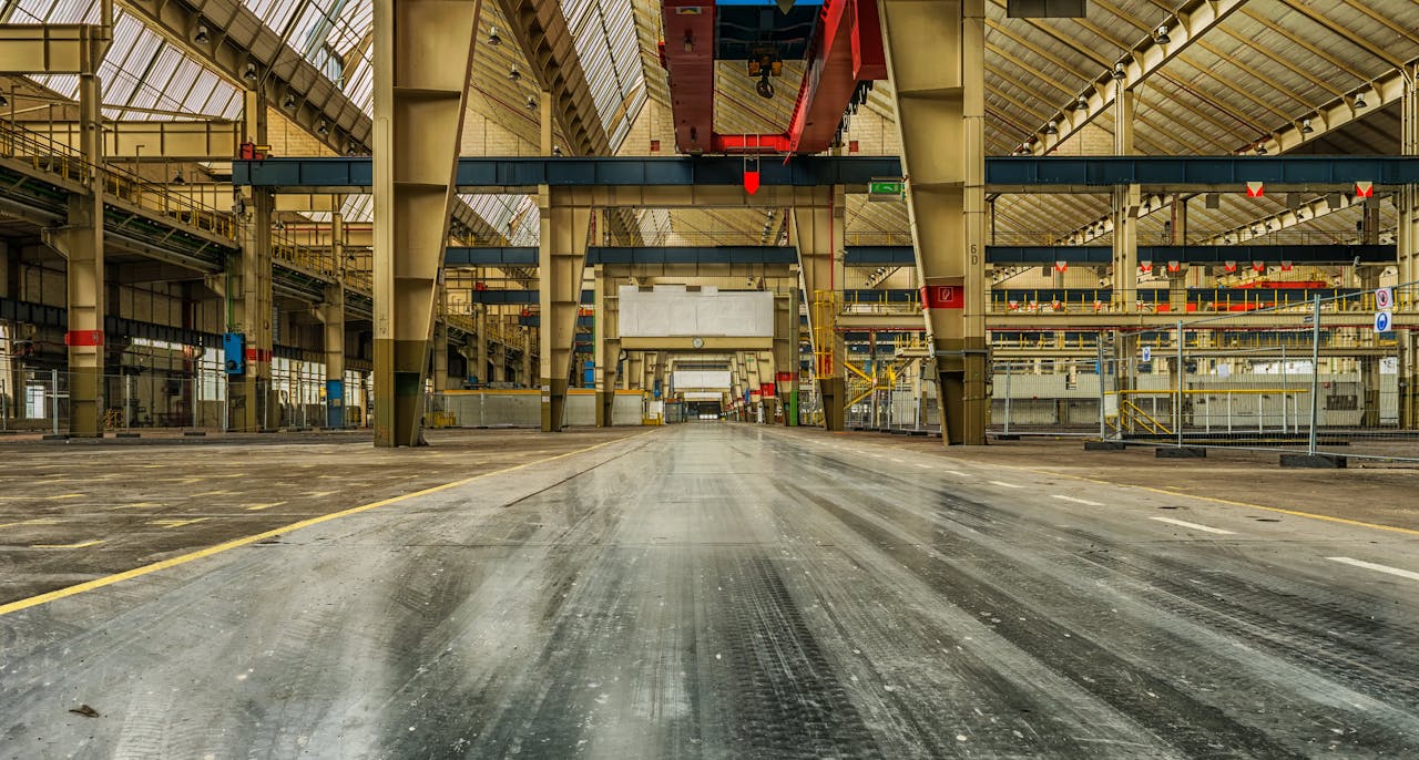 Wide view of an empty industrial warehouse with visible cranes and metal structures.